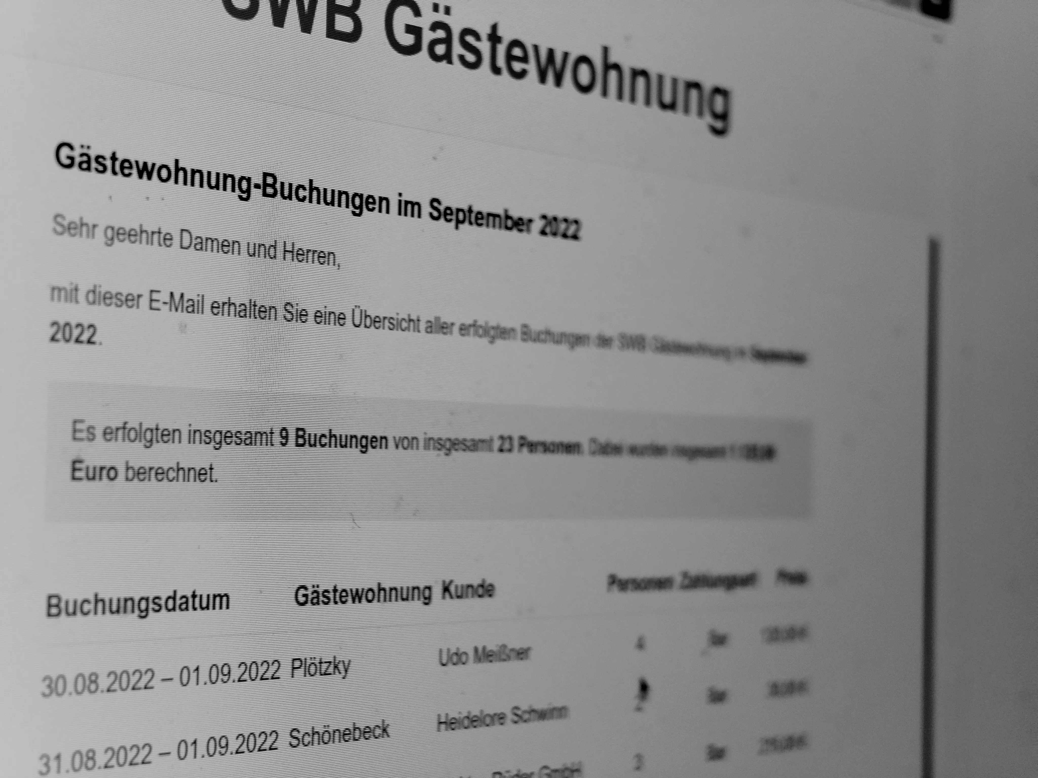 Smartphone and tablet displaying email notification interface for new booking confirmation, modern office desk with coffee cup, property management documents in soft focus background, professional setting, 16:11 aspect ratio, photorealistic